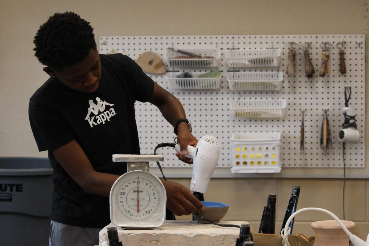 Devin Lewis blow dries a pot during ceramics.