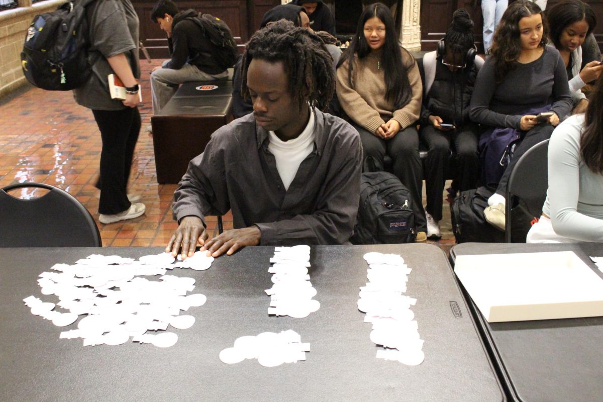 Onyekaorise (Onyeka) Chigbogwu tables for the ETHS Gift Drive, arranging paper snowmen assigned to needed items.